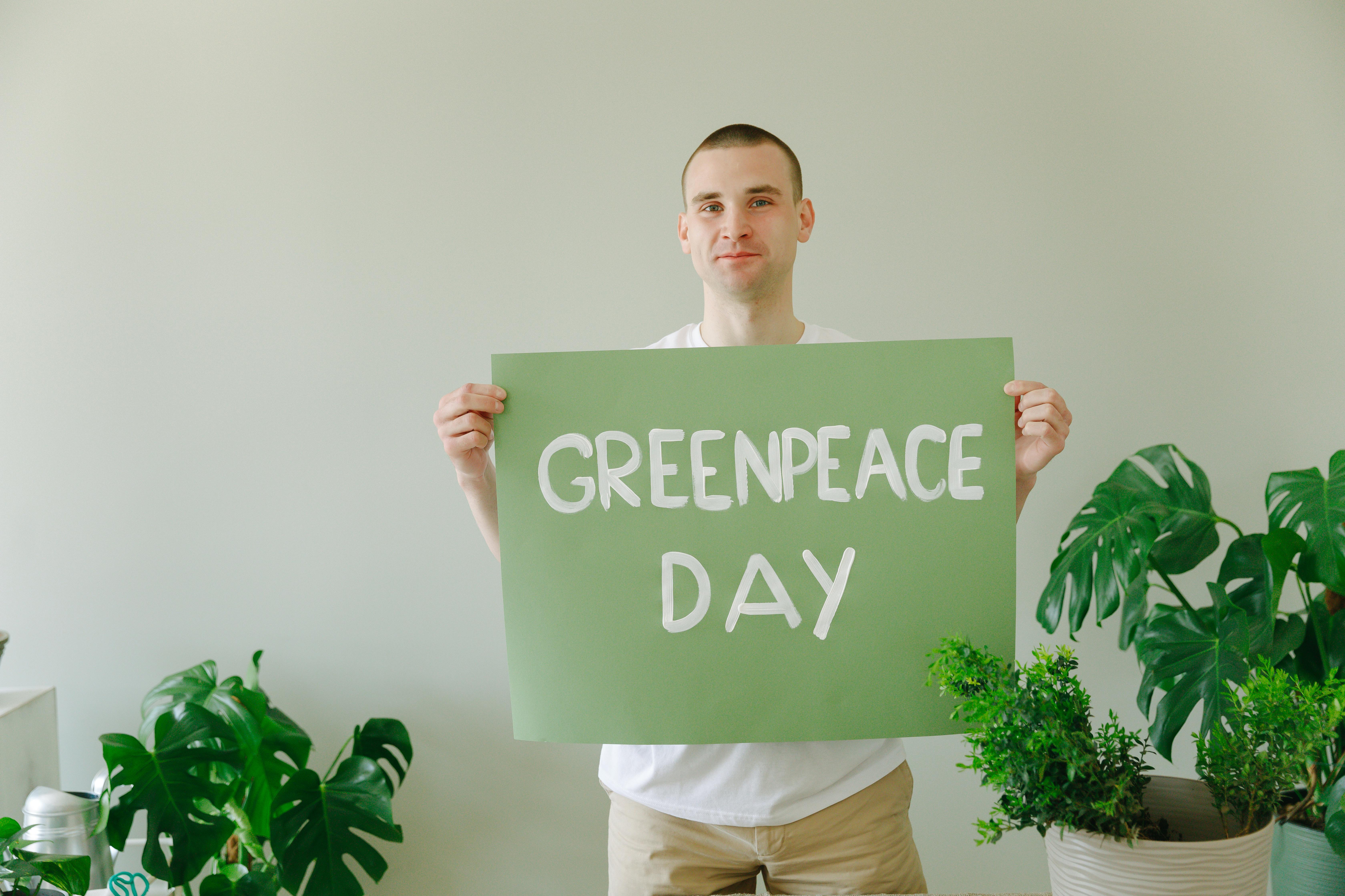 a man holding a green banner with message while standing beside green plants