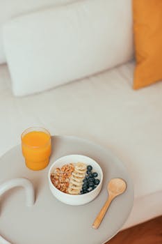 A nutritious breakfast setup featuring granola, banana and blueberry bowl with a glass of orange juice.