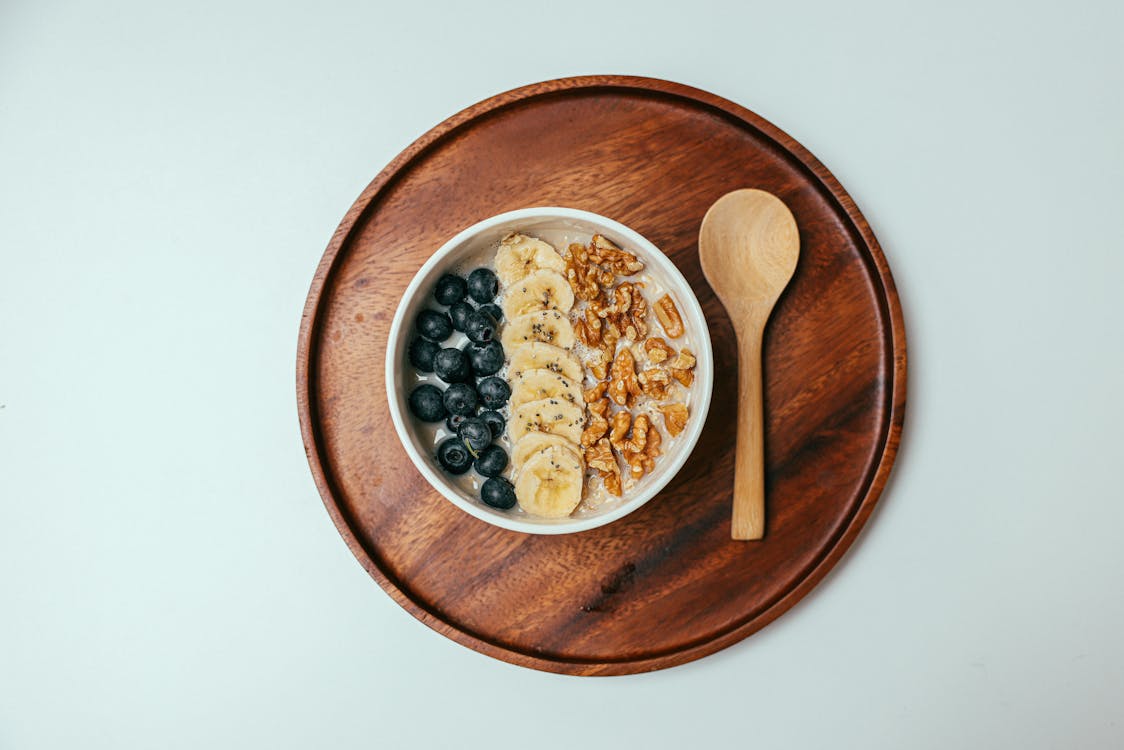 Free A Bowl of Oatmeal Beside a Wooden Spoon on a Wooden Tray Stock Photo
