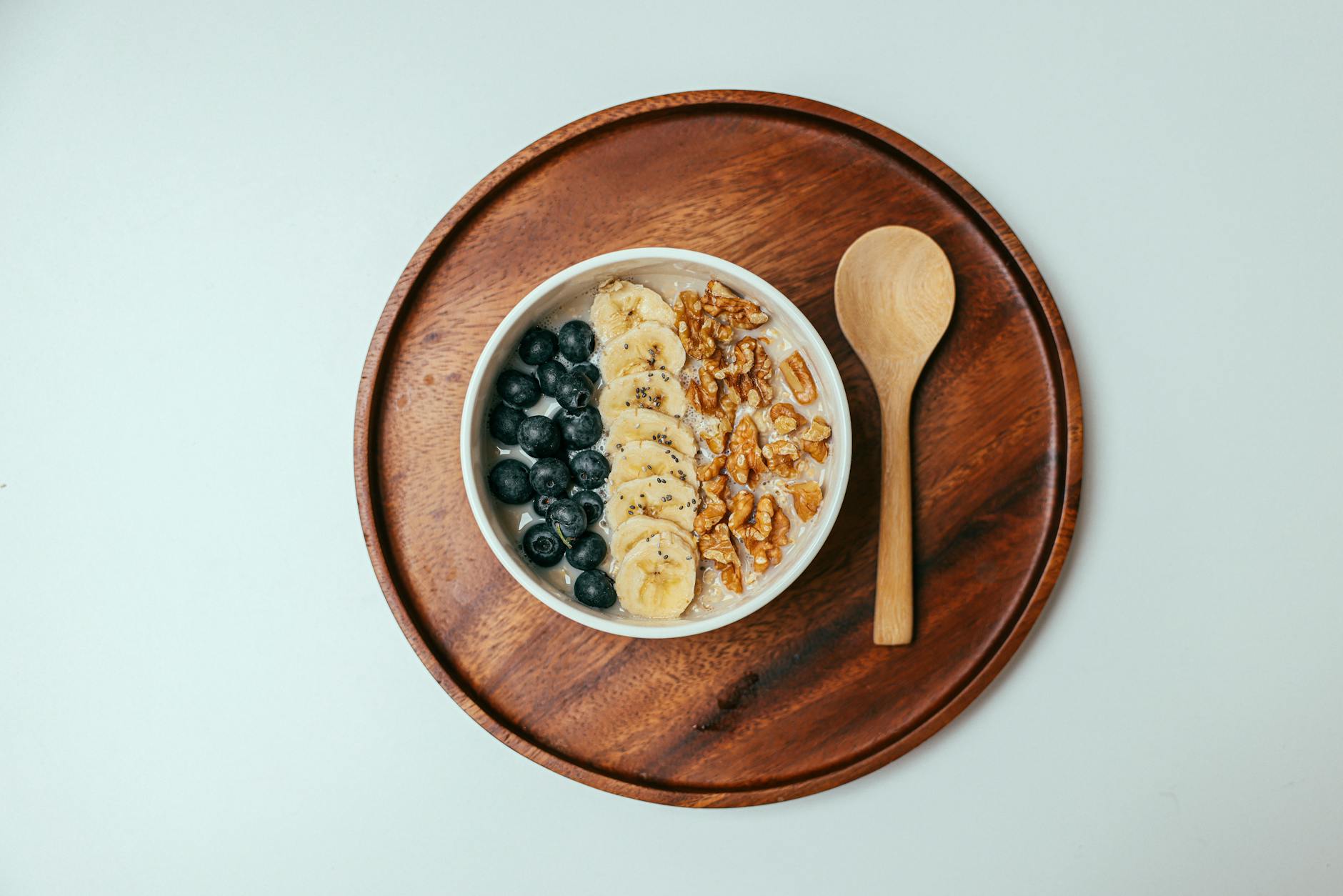 Delicious oatmeal bowl with blueberries, banana, and walnuts on a wooden tray.