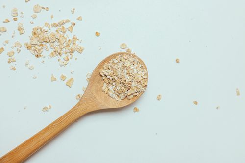 Free High-angle shot of oats spilled from a wooden spoon on a white surface, perfect for health and food themes. Stock Photo