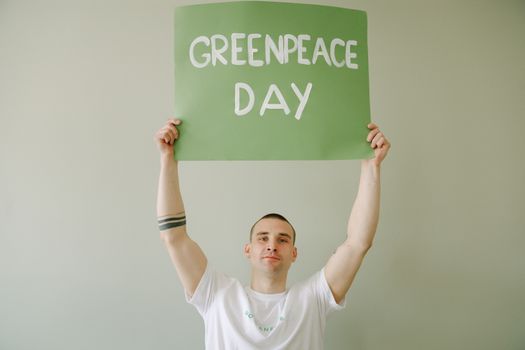 Young man promoting Greenpeace Day with green banner indoors.