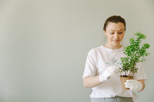 A Woman in White Wearing Gloves while Looking at the Green Plant she is Holding