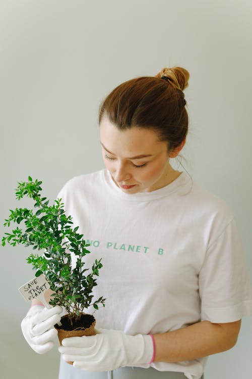 A Woman in White Shirt Looking at the Plant She is Holding