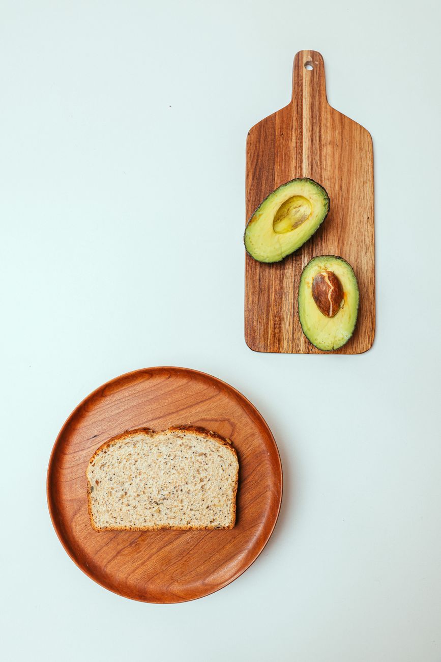 Flat lay of sliced avocado on a cutting board and bread on a plate, perfect for breakfast themes.