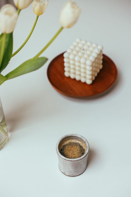 Free A serene minimalist setting with coffee, tulips, and a decorative candle on a wooden plate. Stock Photo