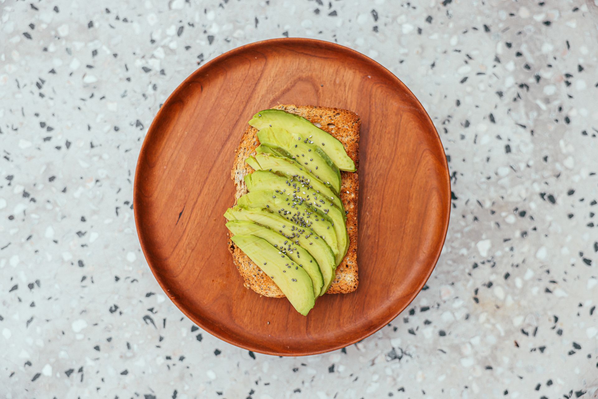 Appetizing avocado toast with chia seeds on a wooden plate, perfect for healthy meals.