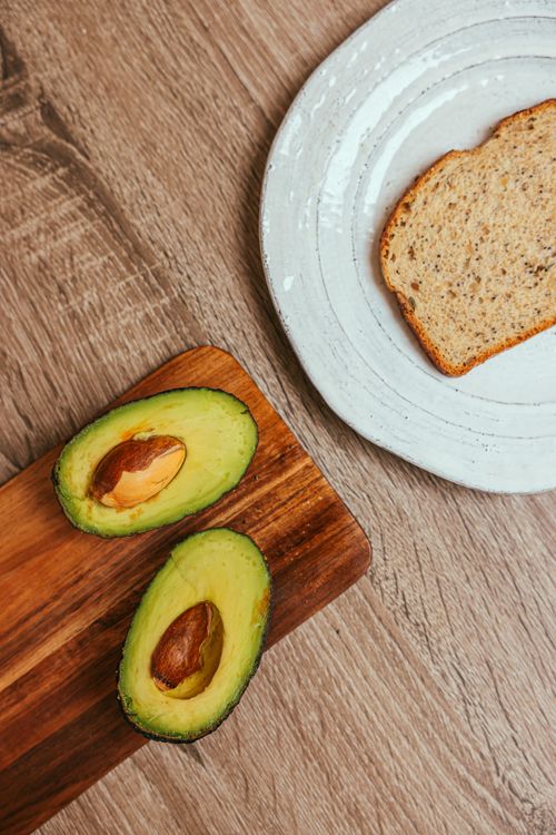 Free Top view of sliced avocado on a wooden board with a slice of bread on a plate. Stock Photo