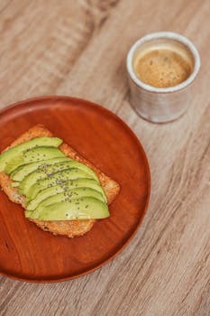 A close-up of avocado toast with chia seeds and a cup of coffee on a wooden table.