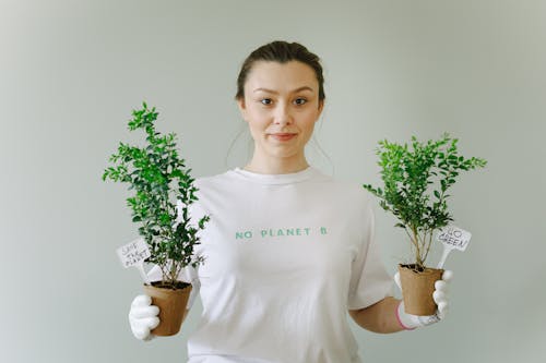 Woman in a White Shirt Holding Plants in Pots