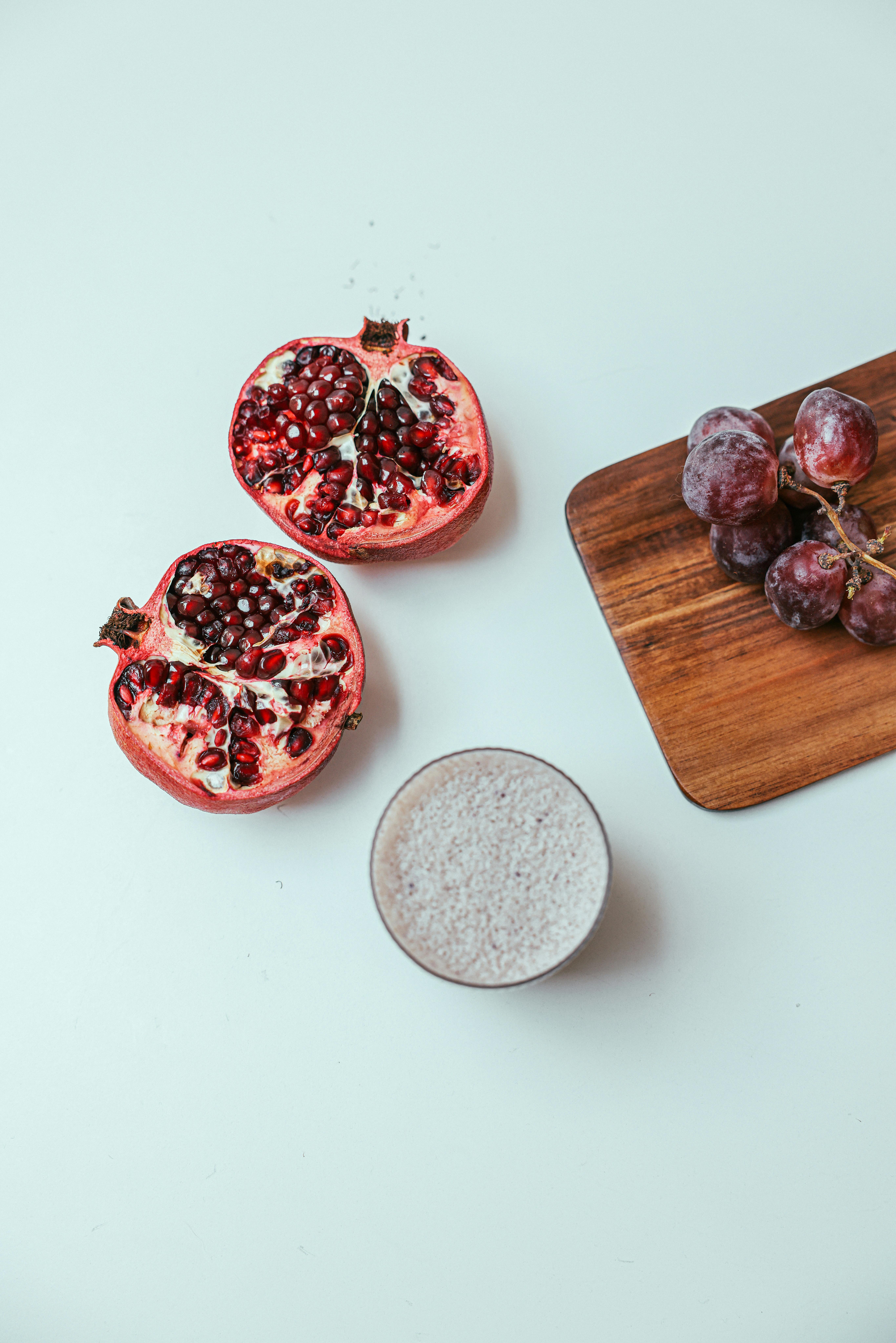 Overhead view of sliced pomegranate, grapes, and smoothie on white surface.