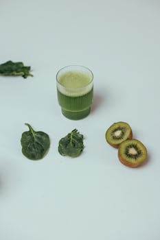 Refreshing green smoothie with fresh kiwi slices and spinach leaves on a white background.