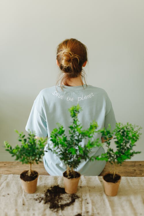 Free Woman Sitting Beside Potted Plants Wearing a Shirt with Save the Planet Text Stock Photo