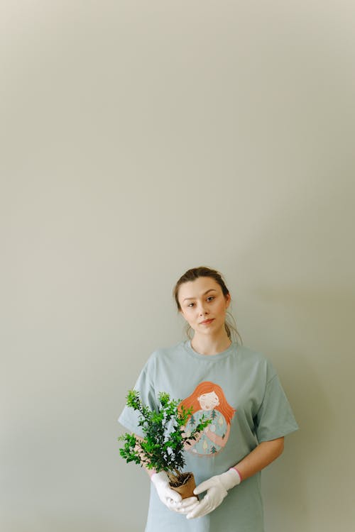 Photo of a Woman with Gloves Holding a Pot with a Plant