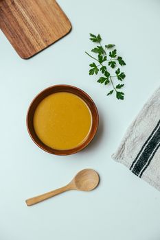Overhead shot of a wooden bowl filled with soup, garnished with parsley, placed on a white surface.