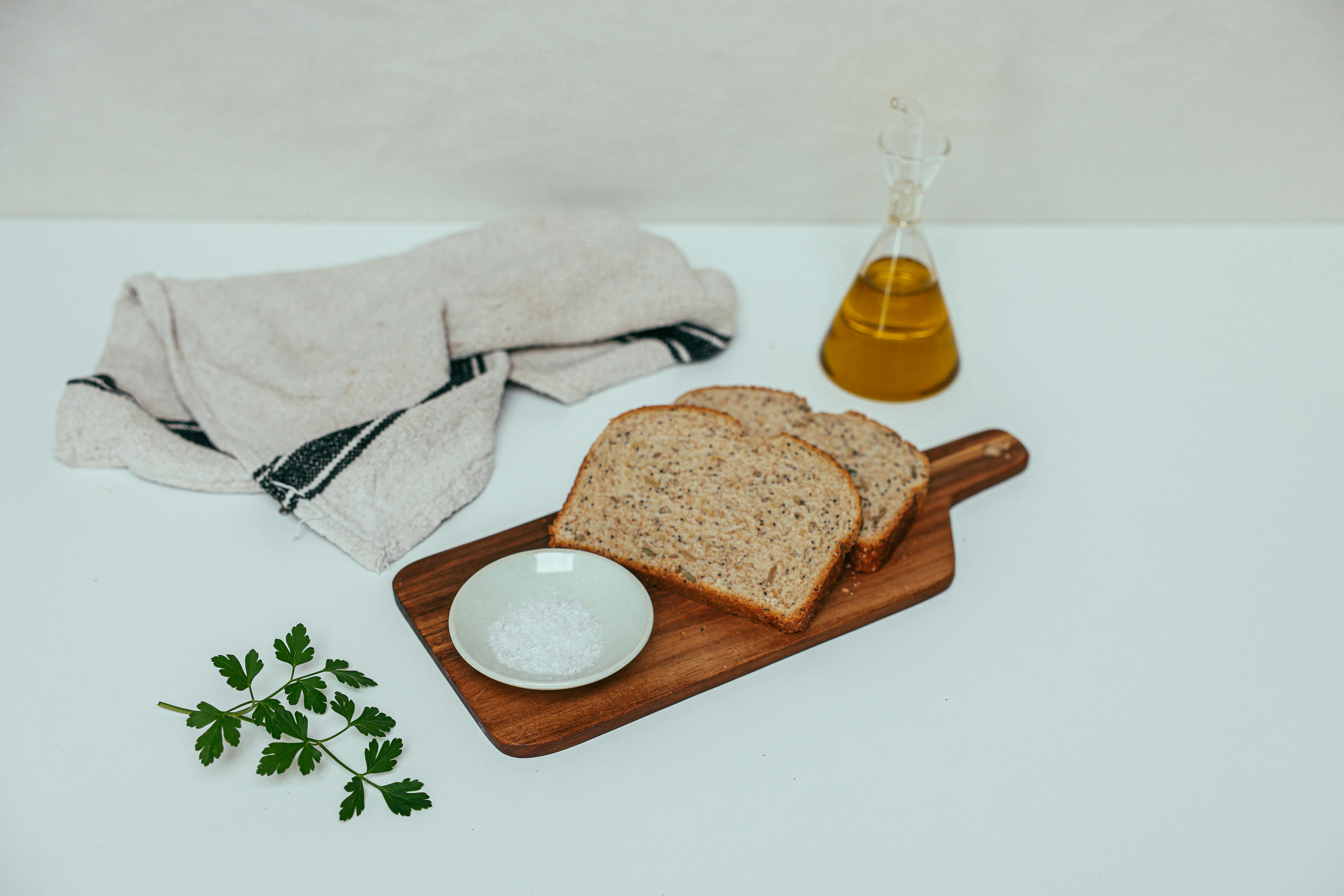 Free Delicious whole grain bread served with olive oil, salt, and parsley on a chopping board. Stock Photo