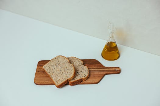 Sliced wheat bread on a wooden board with a flask of olive oil, perfect for a balanced diet.