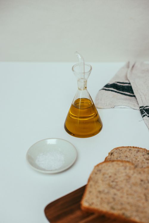 Free Minimalist still life of olive oil, salt, and multigrain bread on white backdrop. Stock Photo
