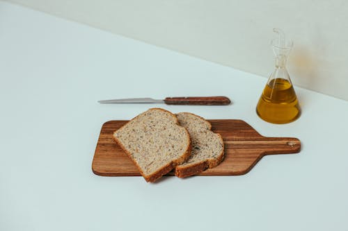 Knife and Olive Oil Beside the Wheat Bread on Wooden Chopping Board