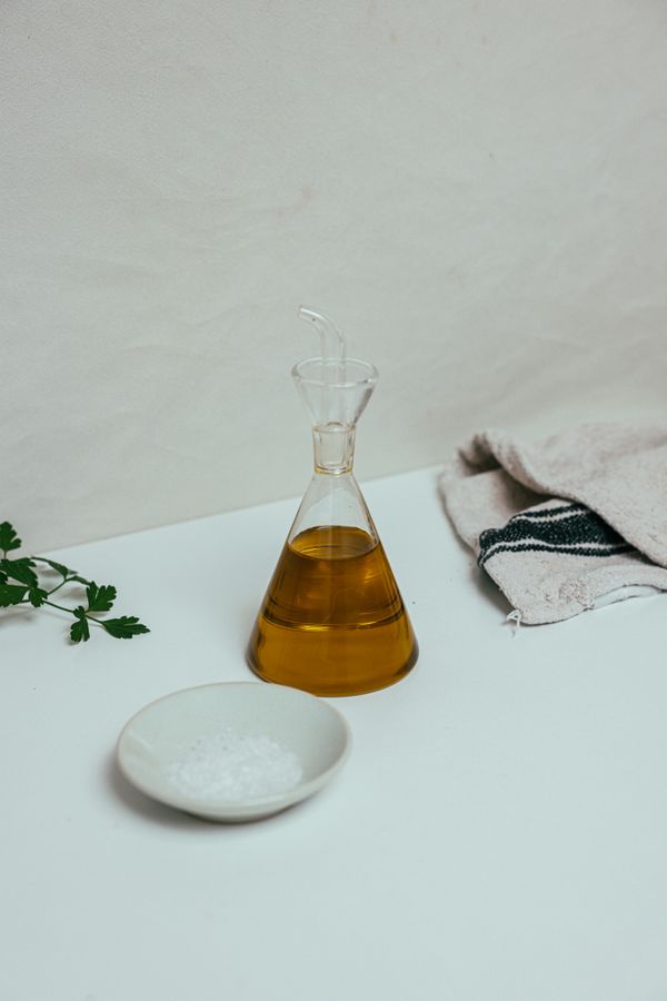 Glass oil bottle on a pale surface, photo by Cup of Couple on Pexels