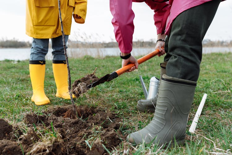 A Person Wearing Grays Rubber Boots Shoveling Ground With Grass