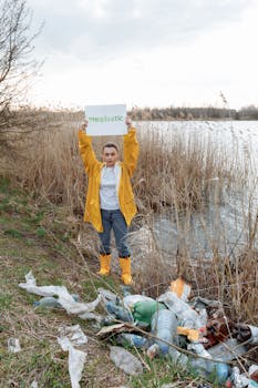 An individual holds a 'stopplastic' sign by a riverbank, highlighting pollution issues.