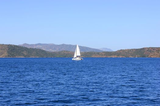 Sailboat gliding on a tranquil lake with mountains in the background under a clear blue sky.