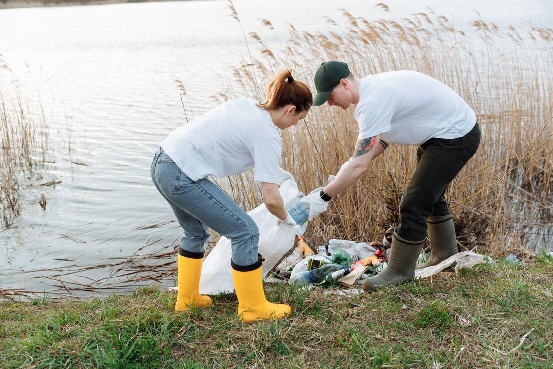Free Two volunteers pick up trash by a river, promoting environmental conservation. Stock Photo