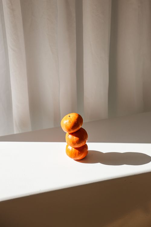 Free A minimalist stack of oranges illuminated by natural light, casting a shadow indoors. Stock Photo