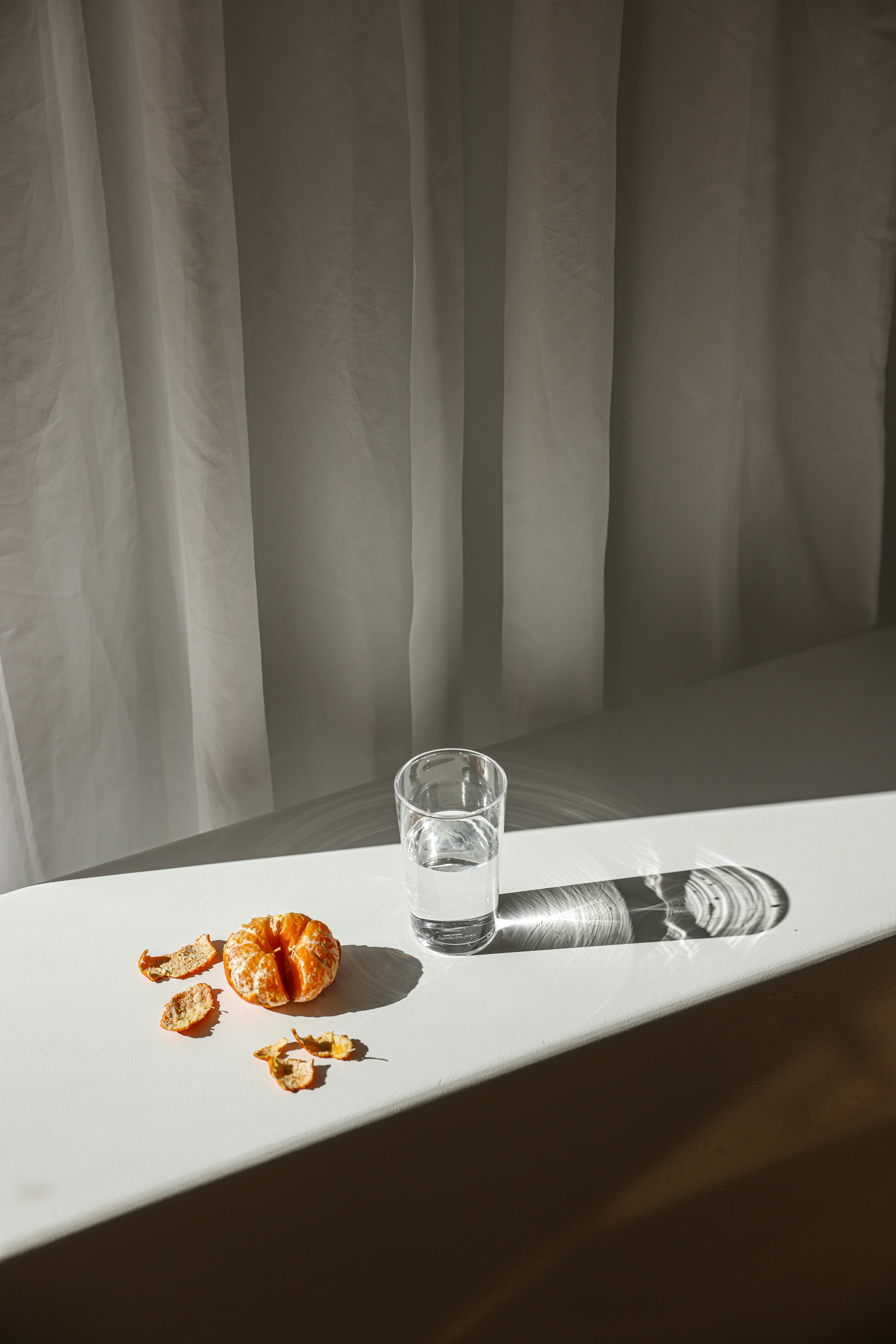 A minimalist scene with a peeled orange and a glass of water casting shadows.