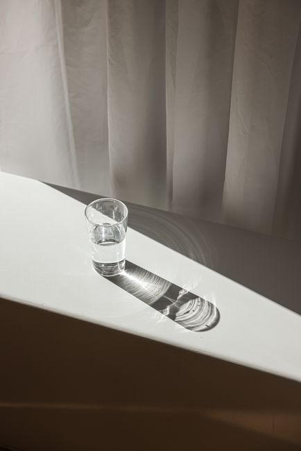A glass of water on a white table casting dramatic shadows in soft sunlight.