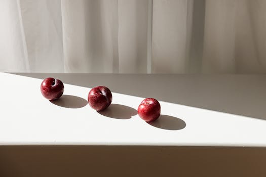 Three red apples casting shadows on white surface with sunlight streaming in.