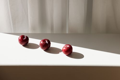 Free Three red apples casting shadows on white surface with sunlight streaming in. Stock Photo