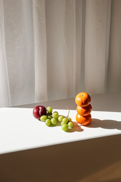 Oranges Green Grapes and a Plum on White Table