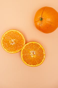 Top view of fresh sliced and whole oranges on a peach background, highlighting their vibrant color and texture.