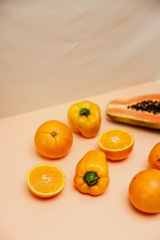 Colorful display of fresh oranges, yellow bell peppers, and papaya slices on a pastel backdrop.