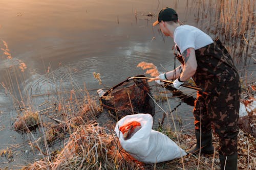 Free A Man Using a Net to Scoop Garbage from a Lake Stock Photo