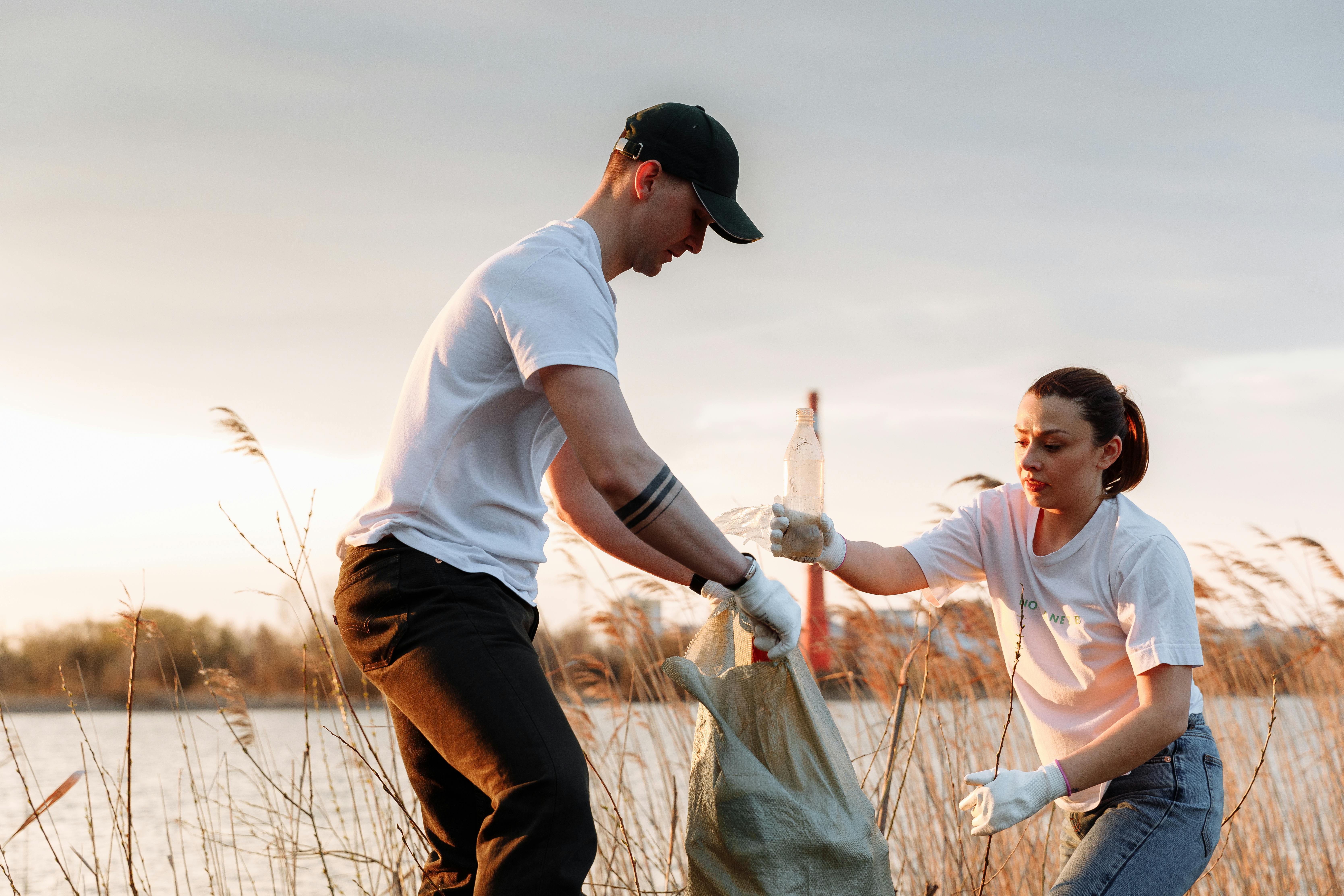 a man and a woman putting garbage in a sack