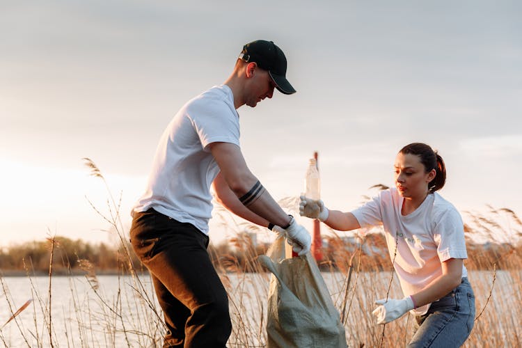 A Man And A Woman Putting Garbage In A Sack