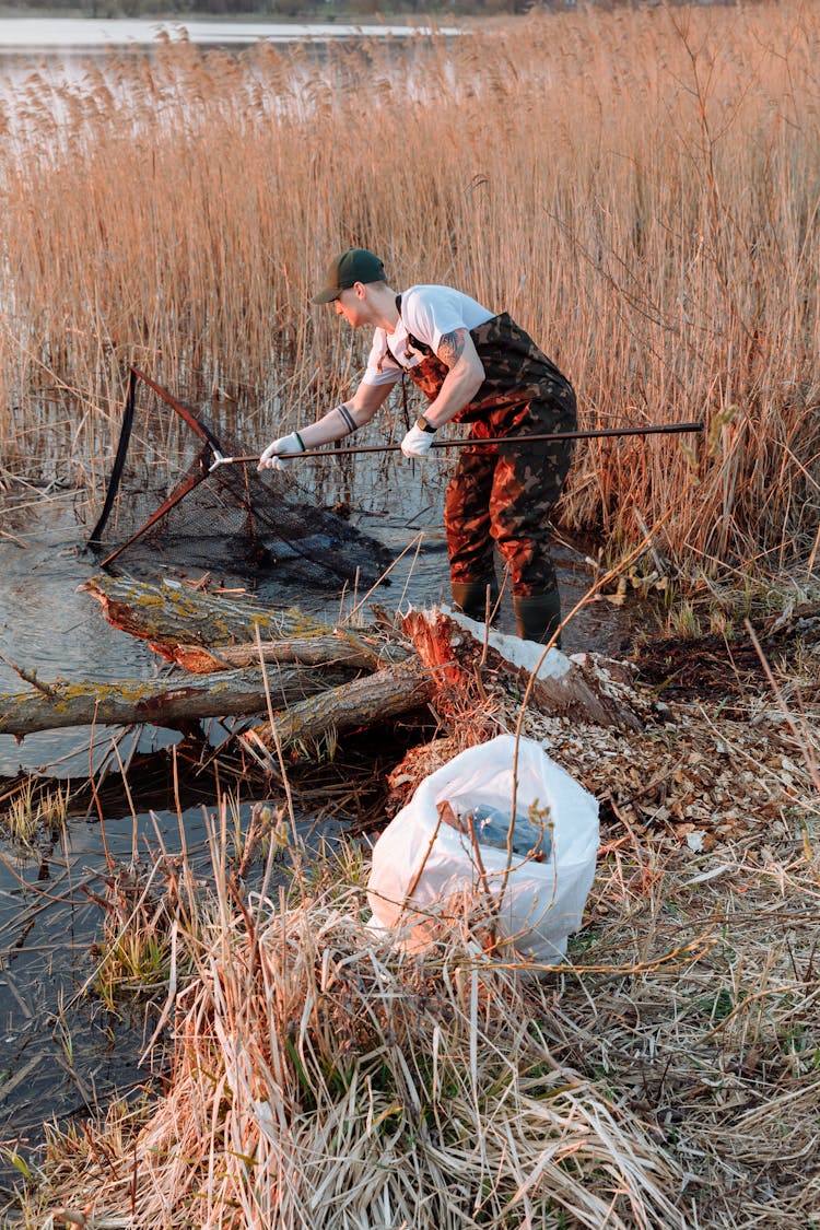 A Man Using A Net While Collecting Garbage In The River