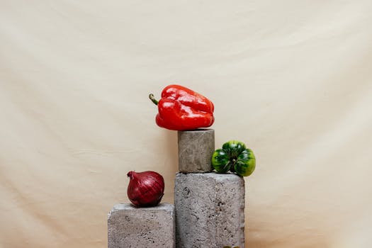 Red bell pepper, green tomato, and onion arranged creatively on concrete blocks.