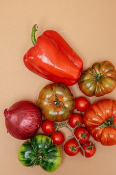 Vibrant assortment of fresh vegetables including tomatoes and bell pepper on a beige backdrop.
