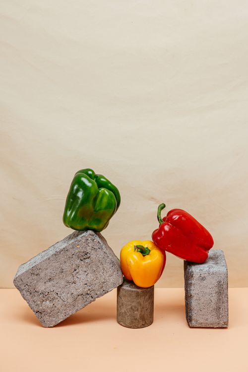Free Vibrant red, yellow, and green bell peppers artfully arranged on concrete blocks. Stock Photo