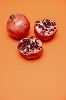 Fresh and juicy pomegranate halves displayed on a vibrant orange background, showcasing their nutritious and delicious appeal.