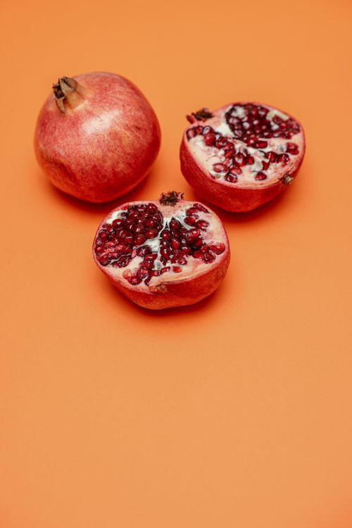 Free Fresh and juicy pomegranate halves displayed on a vibrant orange background, showcasing their nutritious and delicious appeal. Stock Photo