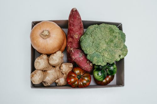 Free Top view of a box containing fresh vegetables including ginger, broccoli, pumpkin, and tomatoes. Stock Photo