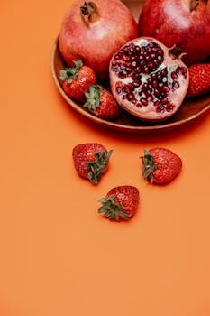 A close-up view of juicy pomegranates and strawberries on an orange background, showcasing fresh, healthy fruits.