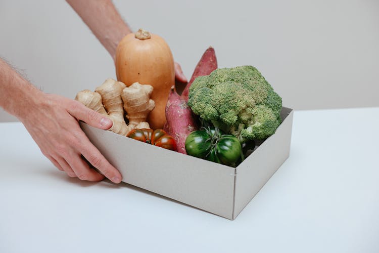 A Person Holding A Box Of Assorted Fruits And Vegetables