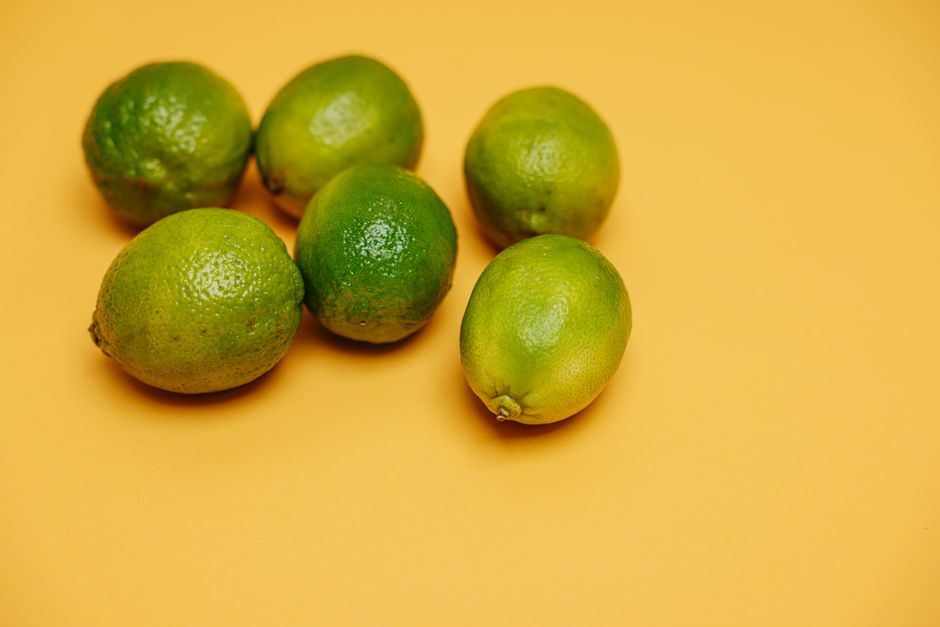 Seis limões verdes frescos em fundo amarelo vibrante, simbolizando frescor e vitalidade.