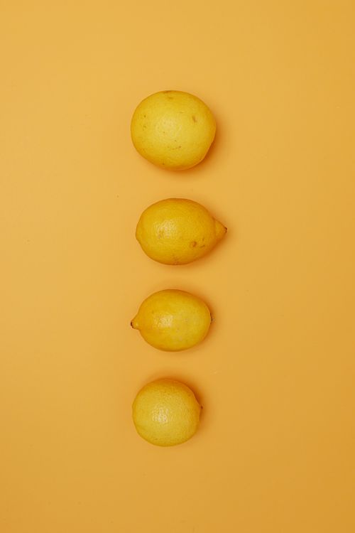 Free Fresh yellow lemons arranged in a vertical line on a bright orange background. Stock Photo